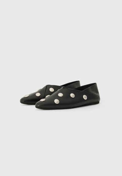 Chaussures plates noires avec un design à bout pointu, présentant de grands accents circulaires en argent sur la surface supérieure et une texture lisse et mate.