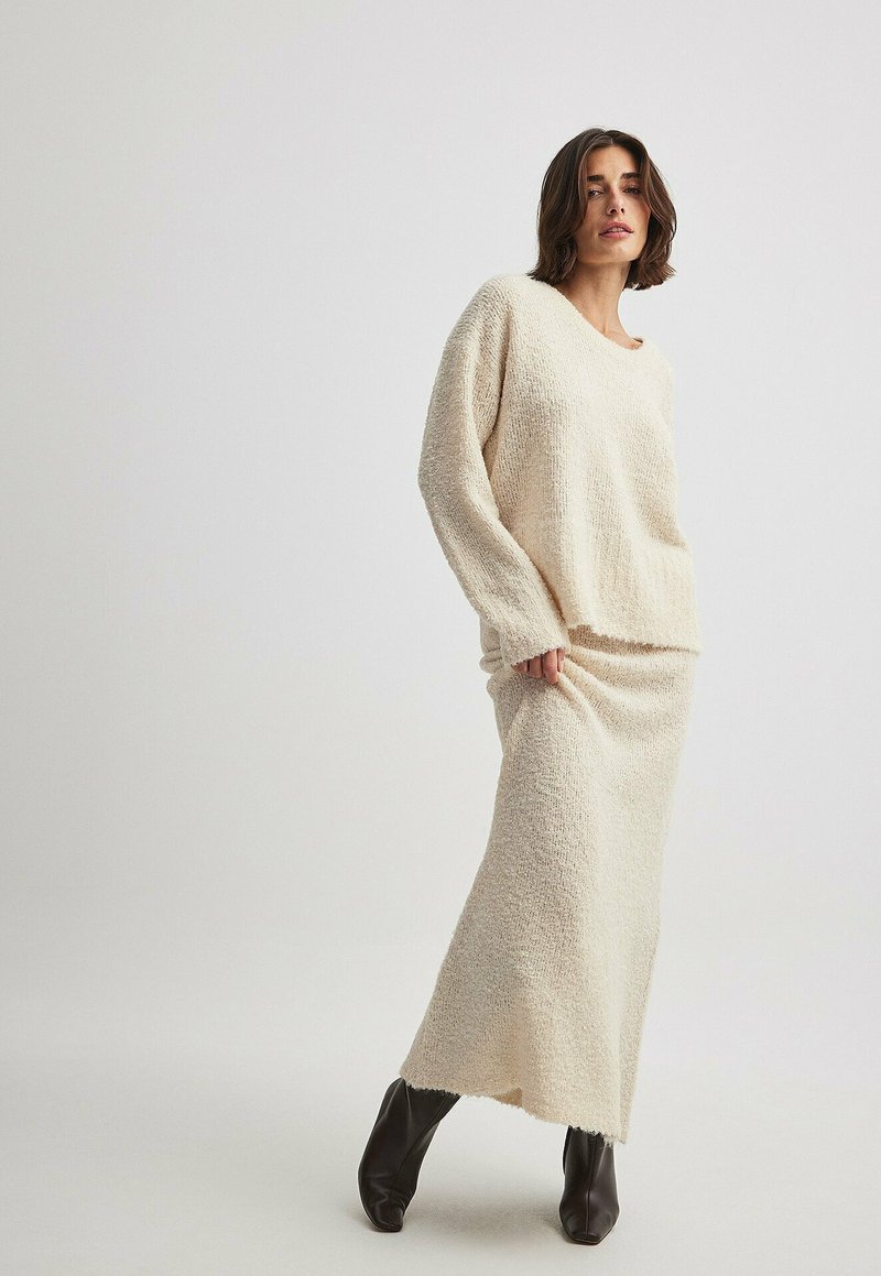 Pull en tricot beige clair et jupe longue assortie, tissu texturé, coupe décontractée, avec un col bateau et des manches longues, associé à des bottes marron foncé.