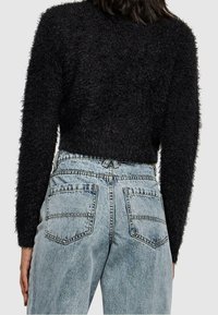 Un pull noir en peluche, court et à manches longues, associé à un jean en denim bleu clair taille haute avec deux poches arrière et des détails de couture.