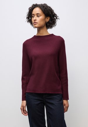 Bordeaux gebreide trui met lange mouwen, ronde hals en een gestructureerde afwerking. Gepaard met donkerblauwe spijkerbroek.