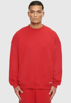 Rotes Sweatshirt mit rundem Halsausschnitt, lockerer Passform, gerippten Bündchen und Saum. Weicher Stoff und minimaler Markenaufdruck auf der unteren linken Seite.