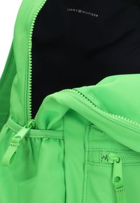 Groene rugzak met een gladde, gestructureerde buitenkant; beschikt over een opvallende ritssluiting en een trekkoorddetail; de binnenkant is zwart. Logo aan de binnenzijde is zichtbaar.