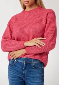 Comodo maglione rosa a maglia con un motivo testurizzato, scollatura rotonda a costine e maniche raglan, abbinato a jeans in denim blu.
