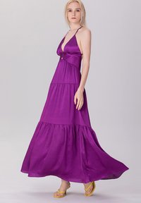 Robe maxi violette avec un décolleté en V profond, design à étages et taille ajustée. Fabriquée en tissu léger ; elle possède des bretelles spaghetti réglables.