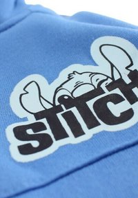 Sweat à capuche bleu à texture douce, avec un motif graphique représentant le visage d'un personnage de dessin animé et le mot « stitch » en lettres noires en gras.
