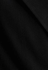Tessuto nero con una texture liscia e opaca, caratterizzato da leggere variazioni di luce dovute a pieghe e grinze. Nessun motivo o hardware visibile.