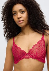 Σουτιέν από δαντέλα σε χρώμα βατόμουρου με κυματιστές άκρες, υποστήριξη με μπανέλα και διάφανο διχτυωτό ύφασμα. Διαθέτει καρδιά-γούνινο στο κέντρο και πιετά διακοσμητικά.