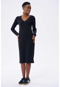 Schwarzes, geripptes Midi-Kleid mit langen Ärmeln und V-Ausschnitt. Kombiniert mit dunklen Turnschuhen mit weißen Streifen. Glatte Textur, figurbetontes Design.