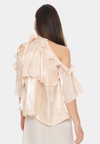 Pale pink, off-the-shoulder blouse with ruffled accents, sheer texture, and layered design. Soft, flowing fabric with a shiny finish.