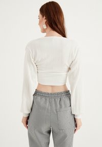 Top corto bianco e texturizzato con maniche lunghe, abbinato a pantaloni a quadri grigi e neri con cintura elastica e tasca laterale.