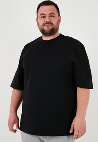 Černé bavlněné tričko s krátkým rukávem, kulatým výstřihem, volným střihem, s hladkým povrchem a bez viditelných vzorů nebo akcentů.