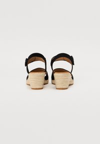 Sandales à talons en suède noir avec une semelle compensée de style espadrille. Présente une bride de cheville avec une boucle. Intérieur lisse et semelle texturée.