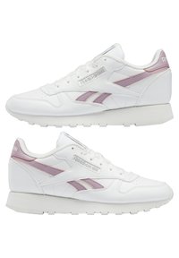 Paire de baskets blanches Reebok avec des bandes de logo violet clair et des accents, lacets blancs et semelles amortissantes, vues de gauche et de droite.