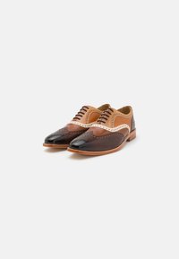 Scarpe in pelle con una combinazione di colori marrone e nero, dettagli brogue, una texture liscia e un design low-profile con lacci.
