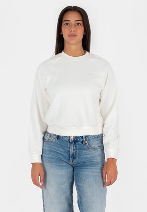 Felpa bianca con scollatura rotonda, polsini e orlo a costine. Abbinata a jeans denim blu, con una leggera scoloritura e chiusura a bottone.