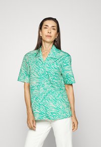 Camisa verde de manga curta com padrão de listras de zebra em branco. Tecido leve, design com colarinho, frente com botões.