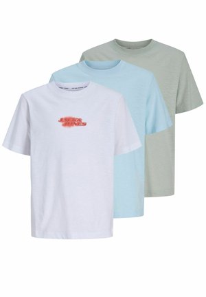 Adolescent garçon debout portant un t-shirt vert clair Jack & Jones, short jaune avec logo, chaussettes blanches et baskets blanches sur fond uni.