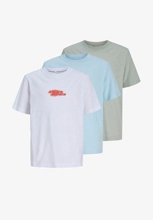 Tinejdžer stoji obučen u svijetlo zelenu Jack & Jones majicu, žute kratke hlače s logom, bijele čarape i bijele tenisice na jednobojnoj pozadini.