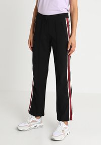 Svarta träningsbyxor med vita och röda sidostråk, med platt midjeband och fickor med dragkedja, bärs med ljusa sneakers.