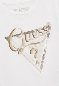 Witte biologisch katoen T-shirt met een driehoekige, goudkleurige paillettenlogo met cursieve tekst en een vraagteken in het midden.