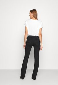 Jeans évasés noirs à taille haute, avec des poches arrière et un tissu lisse et texturé. Associés à un simple t-shirt blanc.