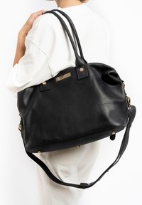 Zwarte leren handtas met dubbele handvatten, verstelbare schouderband, goudkleurige accenten en een textuuraccentstrip aan de voorkant.