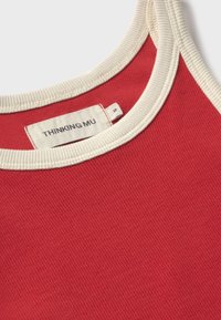 Haut sans manches rouge côtelé avec un bord crème autour de l'encolure et des épaules, montrant l'étiquette de la marque "THINKING MU" et une étiquette de taille petite.
