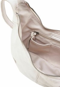 Intérieur d'un sac en cuir beige clair avec une doublure en tissu, comportant une poche zippée et une petite poche plaquée. Texture lisse et forme arrondie.