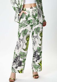 Green and black tropical-print wide-leg pants in lightweight fabric, featuring a high waist, side pockets, and a bold leaf and bird design.