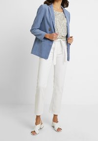 Lichtblauwe linnen blazer met één knop, gecombineerd met een beige met patroon top, witte hoge taille broeken en witte open tenen hakken.