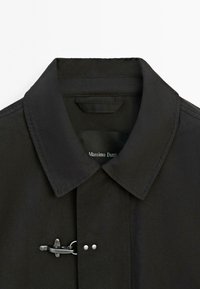 Black shirt with a collar, featuring silver hardware detail and two metallic buttons on the front. Label reads "Massimo Dutti."