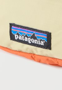 Πατζάκι λογότυπου της μάρκας Patagonia με σχέδιο βουνού ραμμένο σε φόντο από μπεζ και πορτοκαλί ύφασμα.
