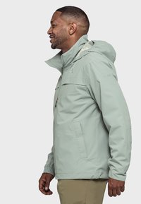 Hellgrüne wasserfeste Jacke mit Kapuze, Frontreißverschluss, Seitentaschen und verstellbaren Bündchen. Mit einem dezenten Logo auf der Brust.