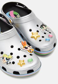 Sabots argentés ornés d'autocollants décoratifs représentant des personnages, des étoiles et des bijoux. Conçus avec des trous de ventilation et un accent de semelle extérieure multicolore.