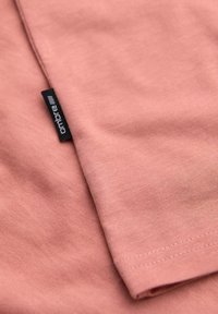 Tessuto in cotone rosa con una superficie liscia, caratterizzato da un bordo piegato e una piccola etichetta nera con il testo "ombre".