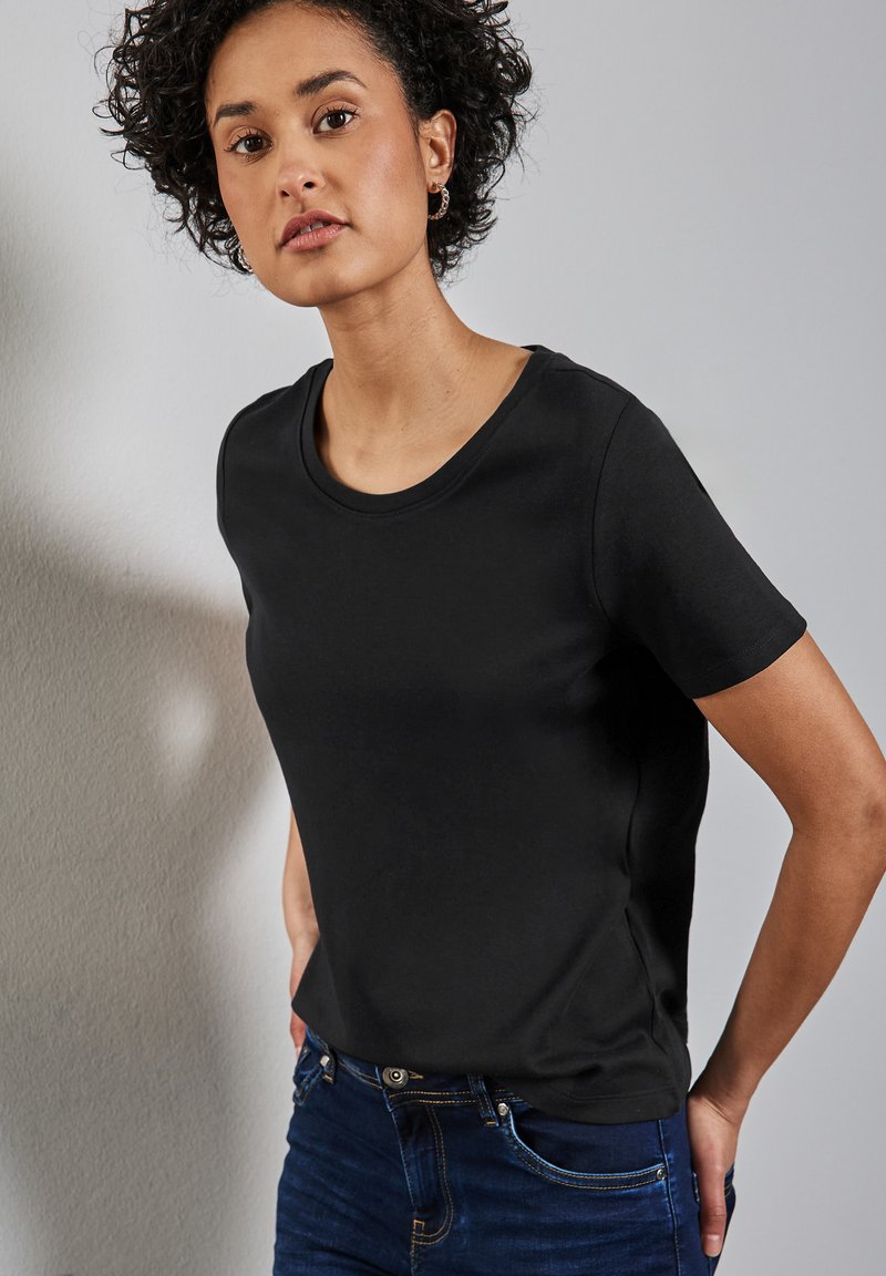 Zwarte korte mouw t-shirt van gladde stof met een ronde hals, gecombineerd met blauwe denim jeans met een getailleerd ontwerp.