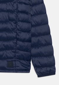 Mörkblå vadderad jacka med quiltat m�önster, som har en gummilogo på den nedre framsidan och elastiska ärmslut för en säker passform.