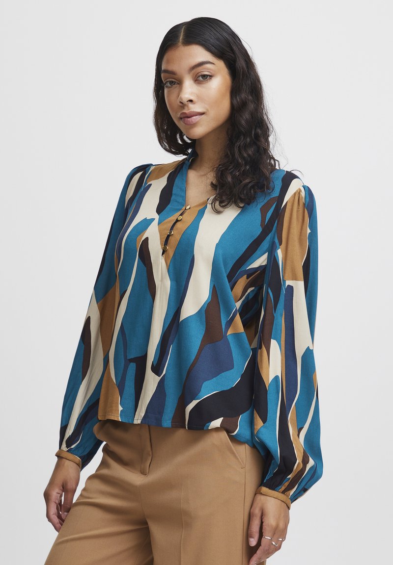 Mehrfarbige Bluse in Blau, Braun und Creme mit abstrakten Mustern. Verfügt über lange Ärmel, einen V-Ausschnitt und Knopfakzente.