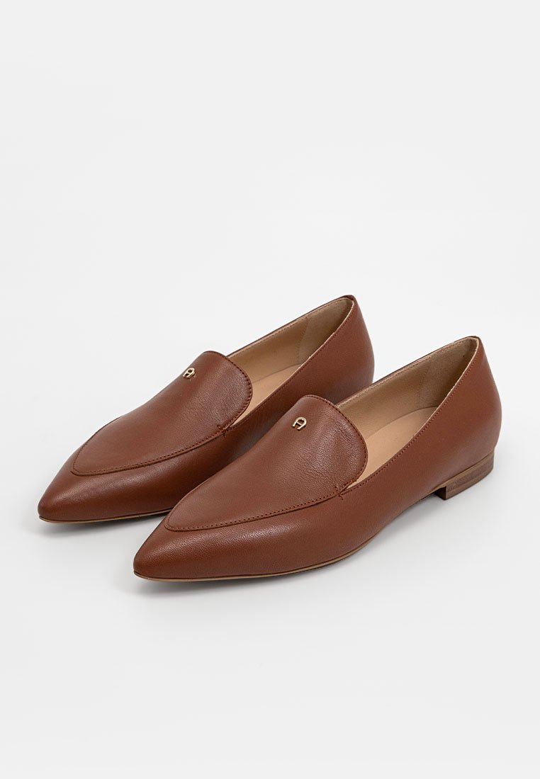 Braune Leder Damenloafers mit spitzem Schuhspitze, niedrigem Absatz und kleinem goldenen Emblem auf der Oberseite, auf einem weißen Hintergrund präsentiert.