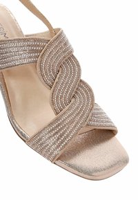 Sandale à bout ouvert avec un dessus en tissu nude orné de bandes entrelacées de strass. Semelle plate avec une finition lisse. Bride ajustable.