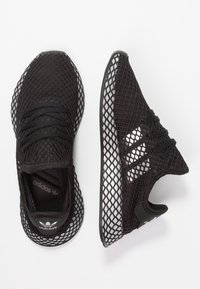 Czarne sneakersy z siateczki o teksturowanym wzorze, z lekką, oddychającą cholewką i trzema białymi paskami po bokach.