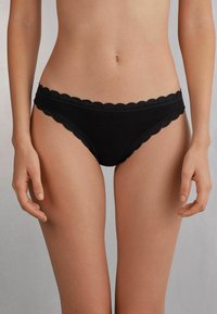 Zwarte katoenen bikinionderbroek met een golvende kantafwerking langs de tailleband en beenopeningen, met een gladde textuur en minimale bedekking.