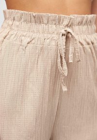 Pantalons à taille élastique en beige clair, avec un motif en grille texturé et un lien à nouer. Tissu doux et léger avec une tombée douce.