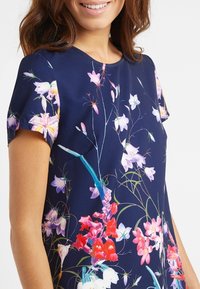 Námořnické květinové šaty s kulatým výstřihem a krátkým rukávem. Tkanina je hladká, zdobená živými vícerozměrnými květinovými vzory.