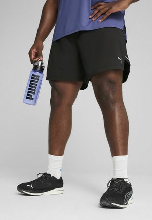 Pantalones cortos deportivos negros, camiseta transpirable morada, zapatillas de correr negras, calcetines tobilleros blancos y una botella de agua transparente azul con logotipo negro.