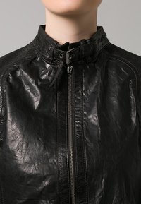 Giacca di pelle nera con colletto alto, zip frontale e finitura testurizzata. Presenta cuciture decorative e una fodera interna liscia.