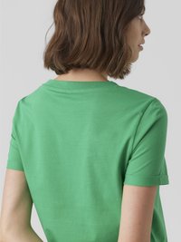 Asmuo su trumpais rudais plaukais, pasukęs šoną, vilkintis ryškiai žalią trumpomis rankovėmis marškinėlį su suktiniu rankovėje.