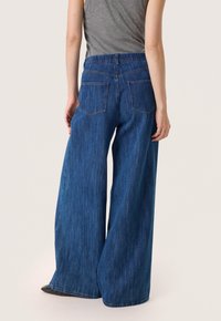 Džíny s širokými nohavicemi z modrého denimu, vysokým pasem, dvěma zadními kapsami a měkkou, texturovanou tkaninou. Lem je rovný a uvolněný.