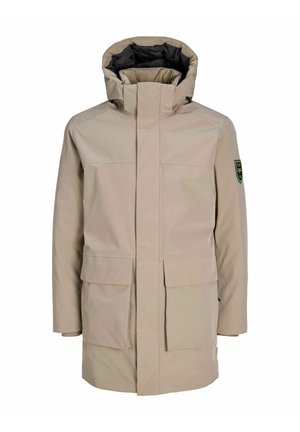 Parka impermeabile beige con colletto alto, due tasche frontali e cappuccio con foderatura interna nera. Emblema verde sulla manica sinistra.