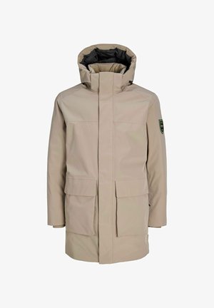 Parka impermeabile beige con colletto alto, due tasche frontali e cappuccio con foderatura interna nera. Emblema verde sulla manica sinistra.
